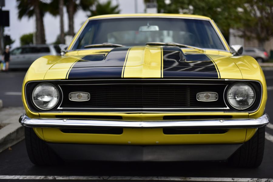 Front view of a yellow muscle car with black racing stripes in a parking lot.
