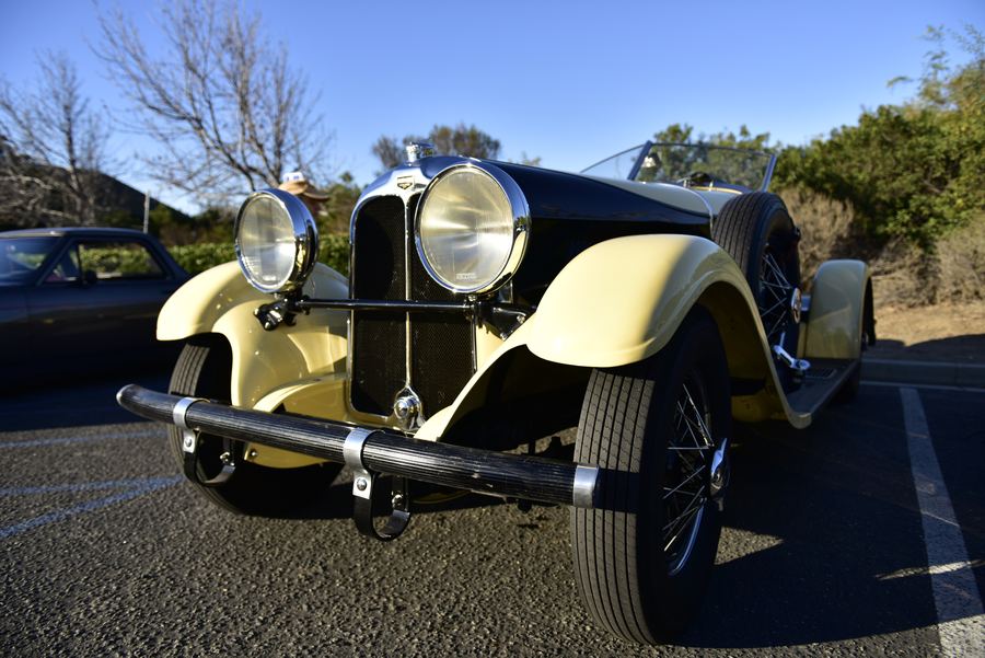 A vintage cream and black roadster with large chrome headlights parked in a lot.
