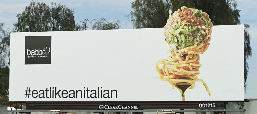 A billboard with a fork twirling spaghetti and a meatball, the hashtag eatlikeanitalian, and a Clear Channel logo below.