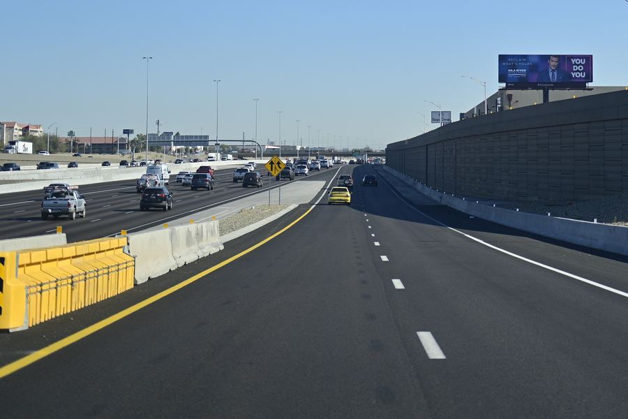Freeway lanes under a clear blue sky, with concrete barriers on the left and a billboard on the horizon at the far right.