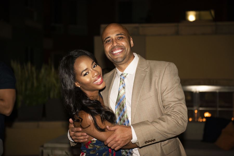 A smiling couple embraces at an evening event. He wears a tan suit and she wears a patterned dress.