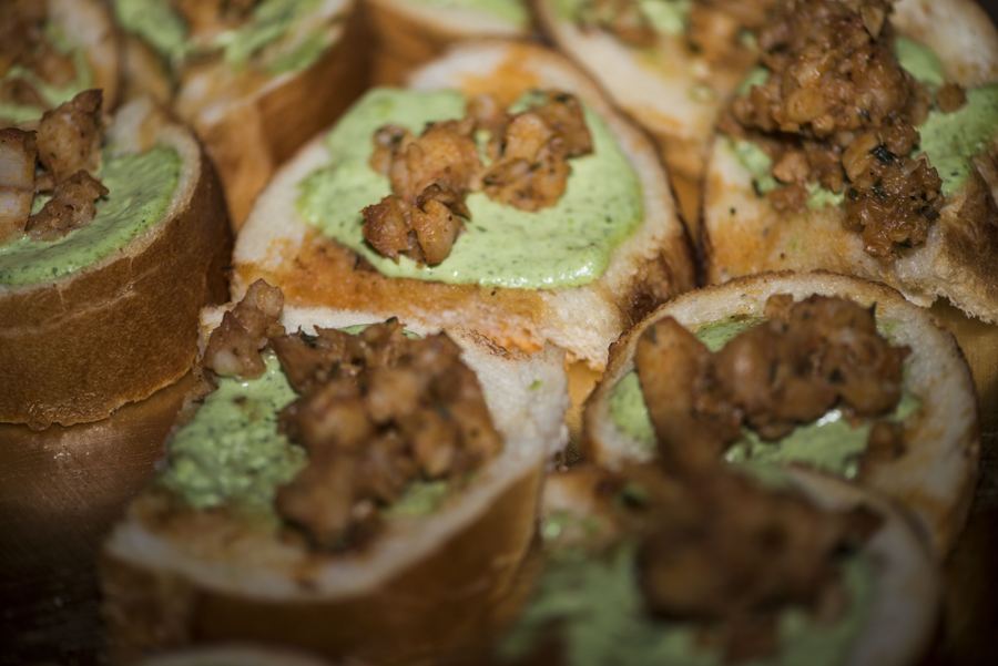 Close view of rolled appetizers topped with green sauce and crumbled meat.