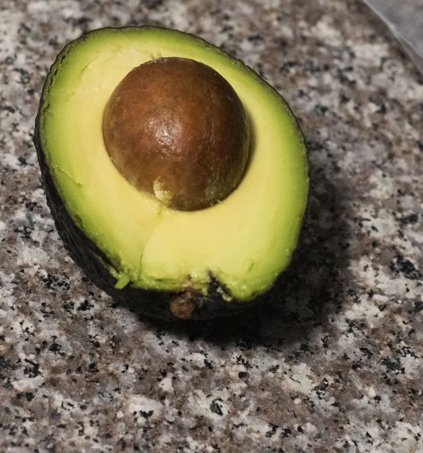 Half an avocado with its pit, lying on a gray granite counter.