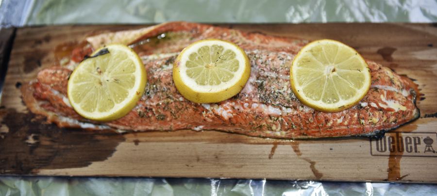 A salmon fillet topped with three lemon slices on a cedar plank.