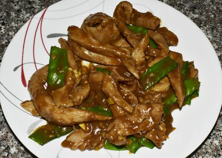 Glazed chicken strips with snow peas on a white plate with a red line pattern.