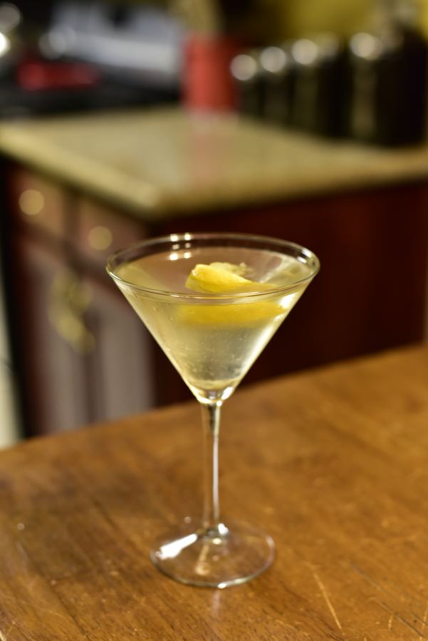 A martini with a lemon twist on a wooden bar.