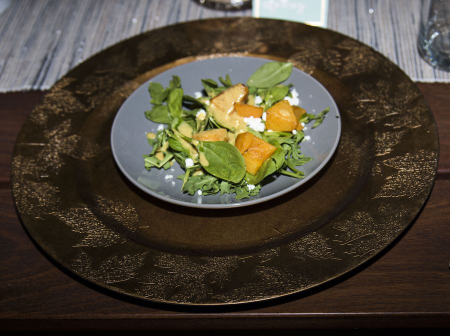 A plated salad of greens, orange segments and cheese on a gray plate set on a dark charger.