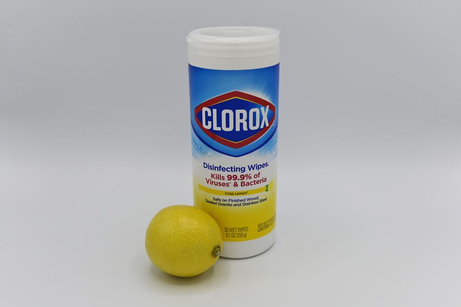 A canister of disinfecting wipes beside a whole lemon on a light gray studio backdrop.