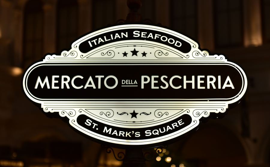 Against a dark background, a lit sign reads Mercato della Pescheria, Italian Seafood, St. Mark's Square.