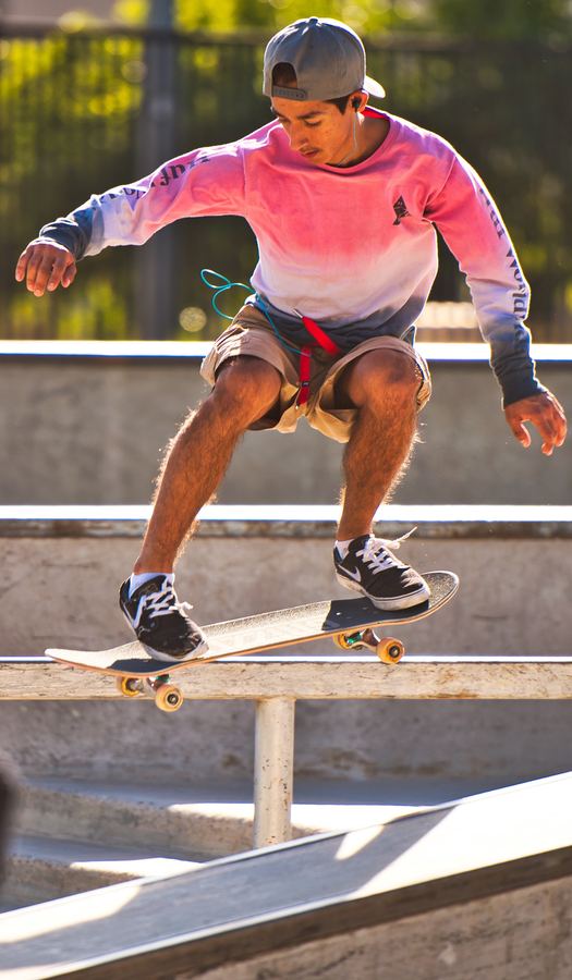 A skateboarder in a pink sweatshirt and cap balances his board on a rail in a concrete skate park.