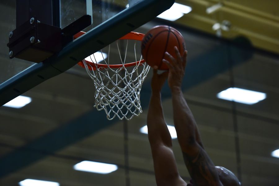 Seen from below, a hand releases a basketball at the rim in an indoor gym.