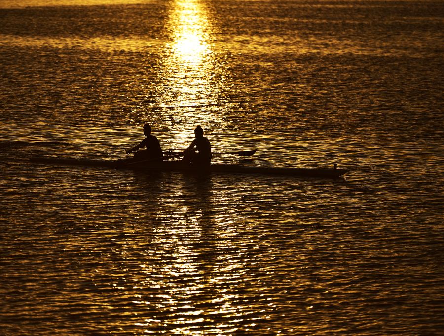 Two rowers in a boat, silhouetted on golden water at sunset.