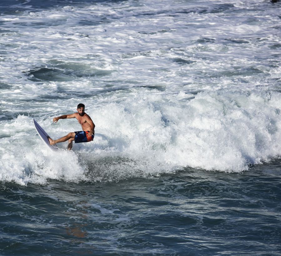 A shirtless surfer turns on a white board in rough whitewater.
