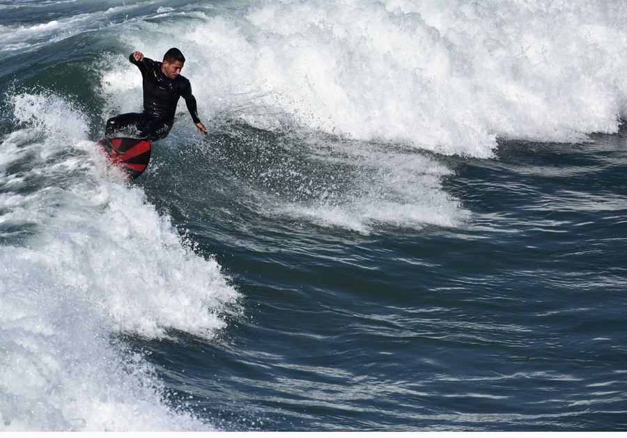 A surfer in a black wetsuit rides down the face of a breaking wave.