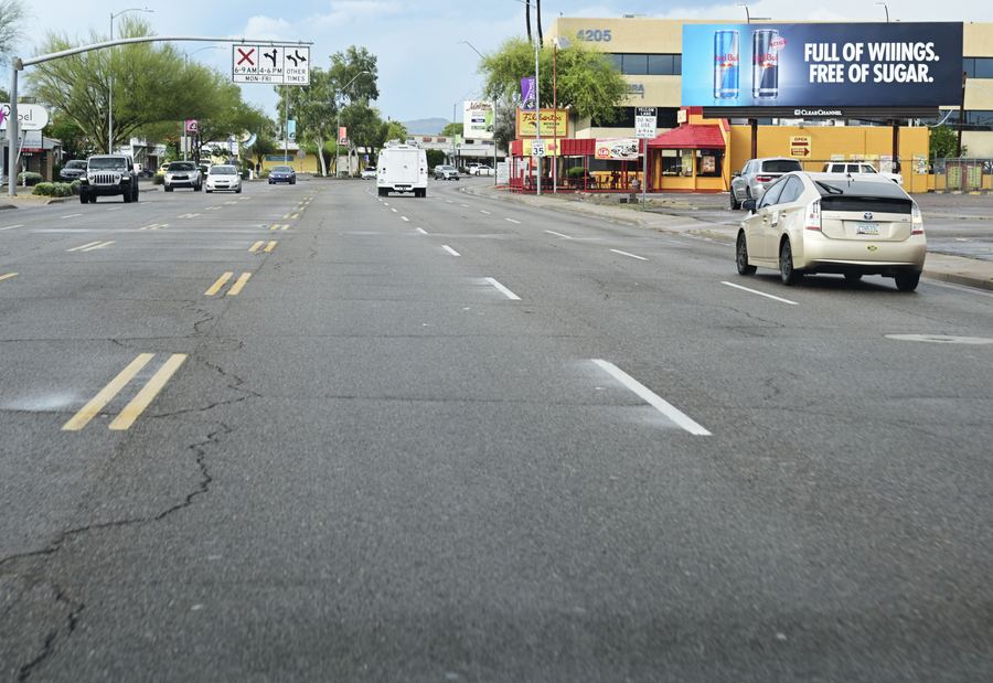 A city street with lanes leading toward a billboard above a row of shops on the right.